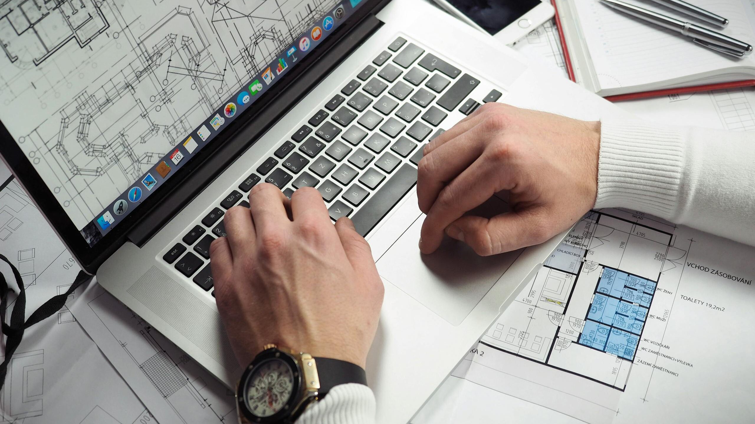 Architect reviewing detailed floor plans and schematics on a laptop with a smartphone nearby.